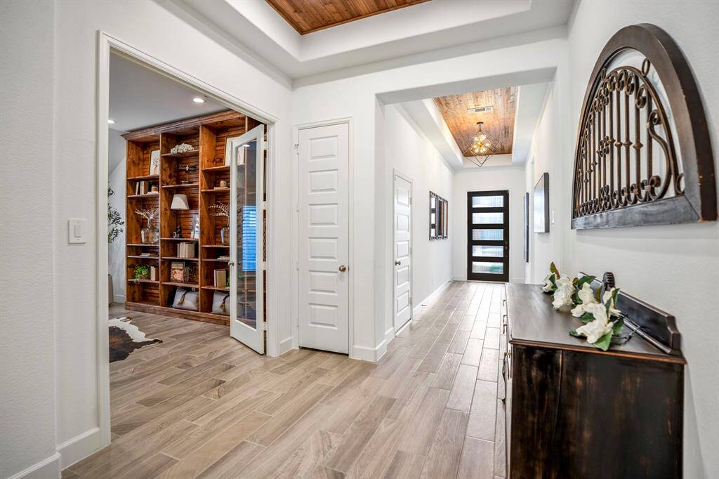 A sleek, black-framed front door with frosted glass panels allows natural light to filter through while maintaining privacy. The hallway is wide and inviting, connecting to various rooms and creating a seamless flow between spaces. As you enter on the right you will notice the beautiful home office space and on the left the elegant wine grotto.