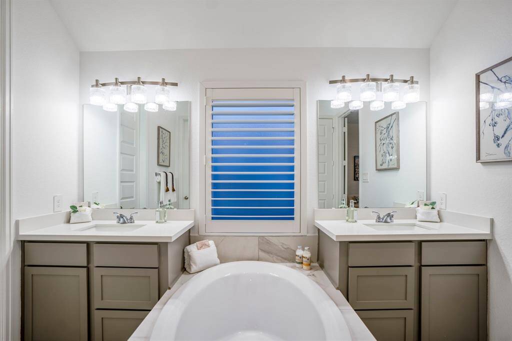 Two separate vanities with gray cabinetry and white countertops, offering plenty of storage and personal space.Large framed mirrors above each vanity, accompanied by modern light fixtures with glass shades for a bright, polished look.