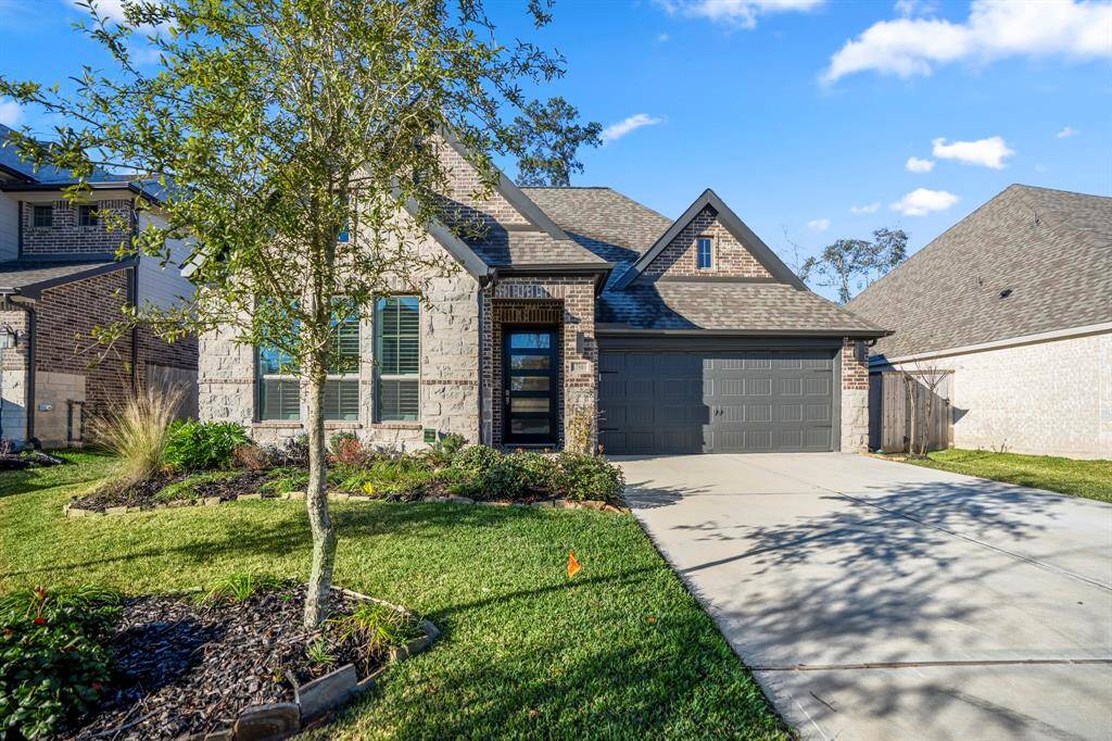 A well-maintained front yard with lush green grass and neatly arranged flower beds adds curb appeal. Shrubs, flowering plants, and ornamental grasses enhance the landscape's texture and color, and a young tree in a mulched bed.