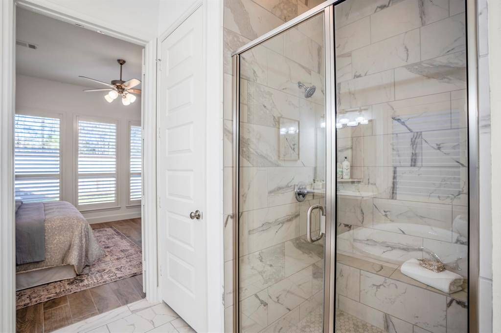 A frameless glass-enclosed k-in shower with marble-inspired tile walls, blending seamlessly into the design.