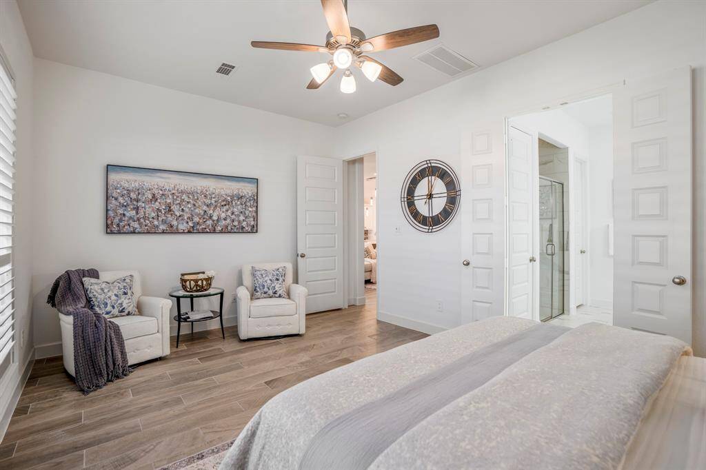 Wood-look tile flooring extends throughout the room, offering durability and a clean aesthetic. A cozy corner features cream armchairs with blue floral pillows and a side table, perfect for relaxing with a book or enjoying morning coffee.