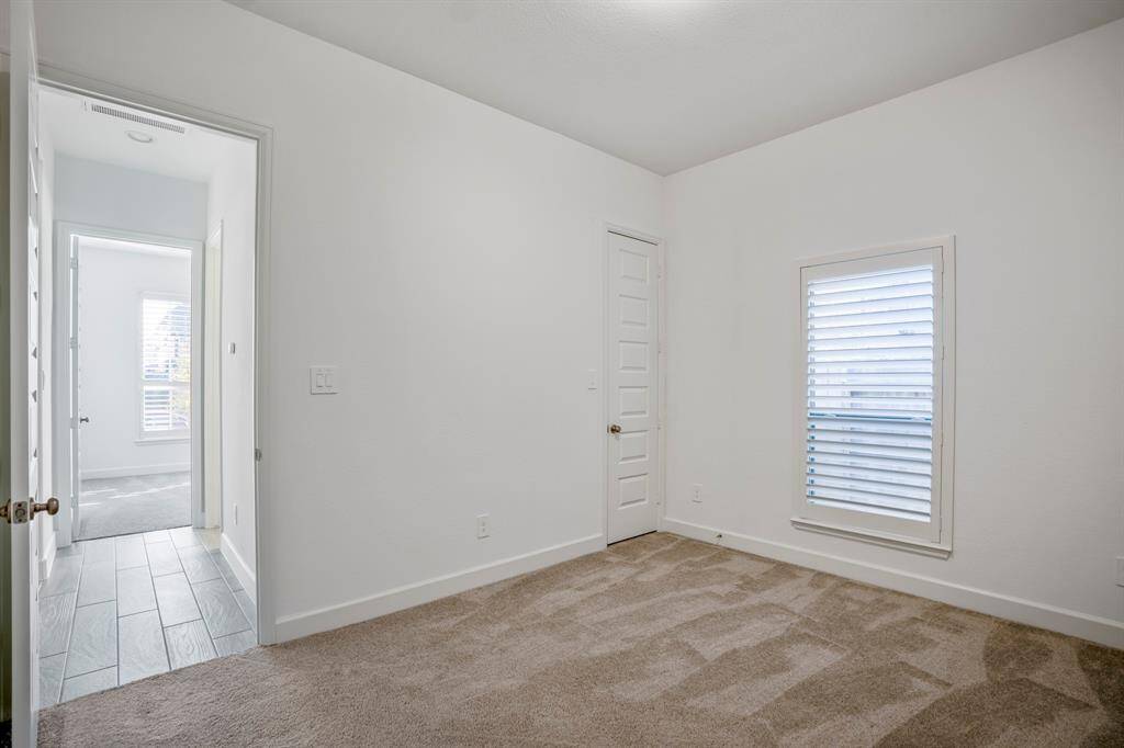 This secondary bedroom is versatile and functional, making it suitable for a guest room, child’s bedroom, or home office. A single window with plantation shutters provides natural light while maintaining privacy. The view adds brightness and a connection to the outdoors. The room is connected to a shared hallway with wood-look tile flooring, ensuring seamless transitions between spaces.