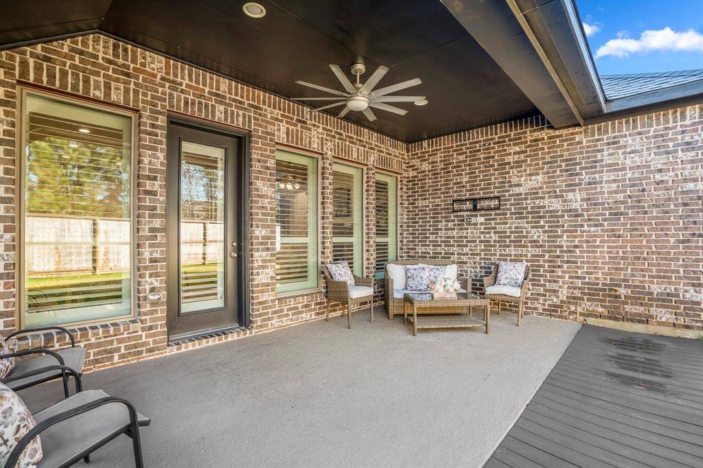A spacious covered area with a dark ceiling and built-in fan for comfort and shade, making it ideal for year-round use. A classic brick wall provides a timeless and durable backdrop, adding character to the space.A wicker seating set with plush cushions and floral accent pillows creates a welcoming and comfortable sitting area.A matching glass-top coffee table adds functionality for outdoor meals or drinks.