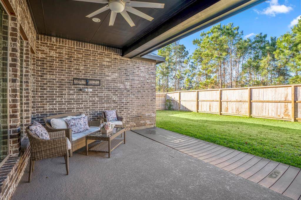 A spacious covered area with a dark ceiling and built-in fan for comfort and shade, making it ideal for year-round use. A classic brick wall provides a timeless and durable backdrop, adding character to the space.A wicker seating set with plush cushions and floral accent pillows creates a welcoming and comfortable sitting area.A matching glass-top coffee table adds functionality for outdoor meals or drinks.