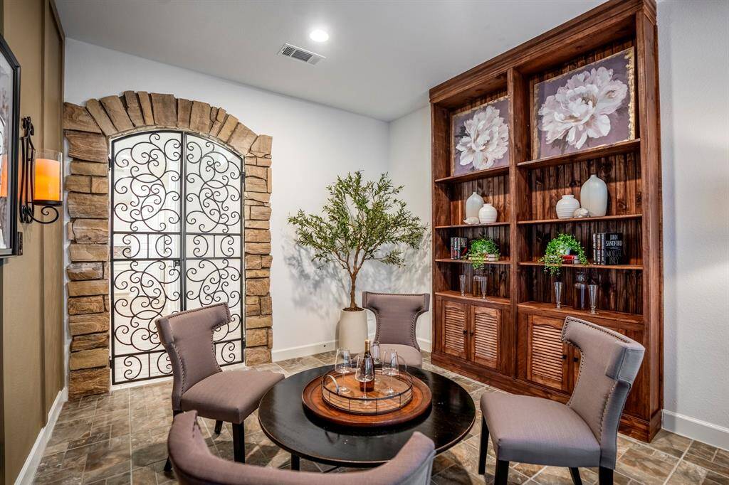 This a custom wine grotto featuring large wooden built-in shelving unit displays a mix of decorative items such as vases, framed floral artwork, greenery, and books, contributing to a personalized and sophisticated touch. The flooring is tiled in a natural, stone-like finish, enhancing the earthy and refined atmosphere.
