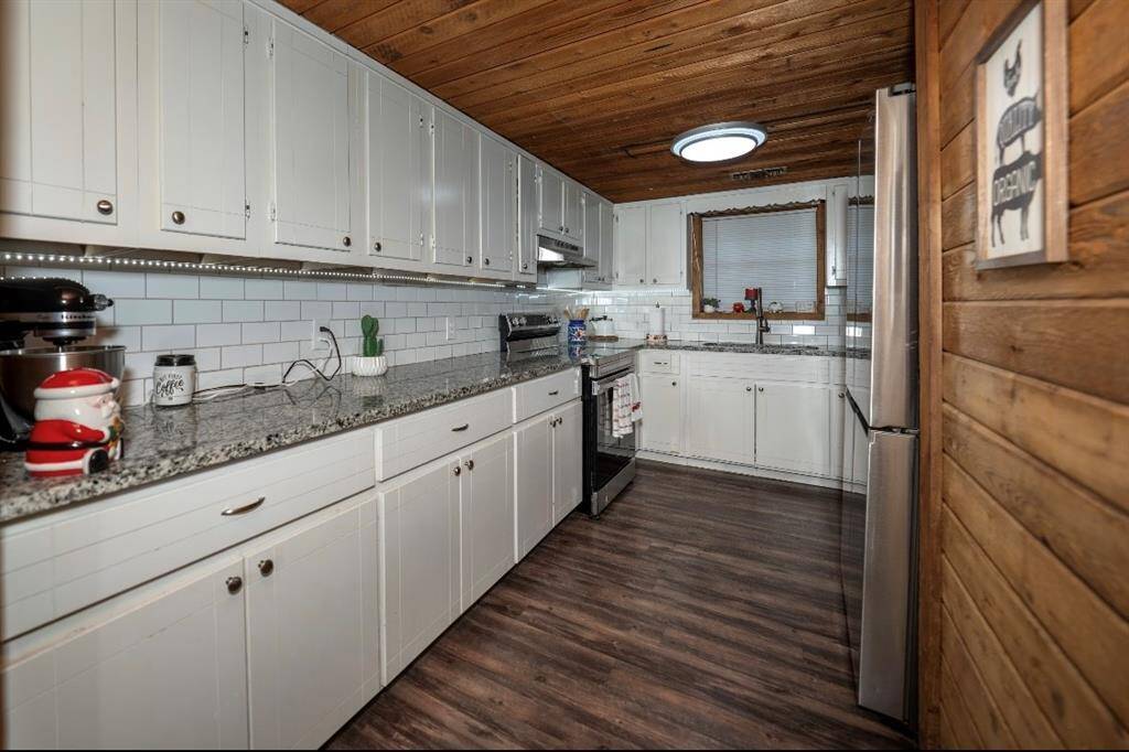This cozy kitchen features white cabinetry, granite countertops, and a stainless steel stove. It has a wooden ceiling with a modern light fixture, creating a warm and inviting space.