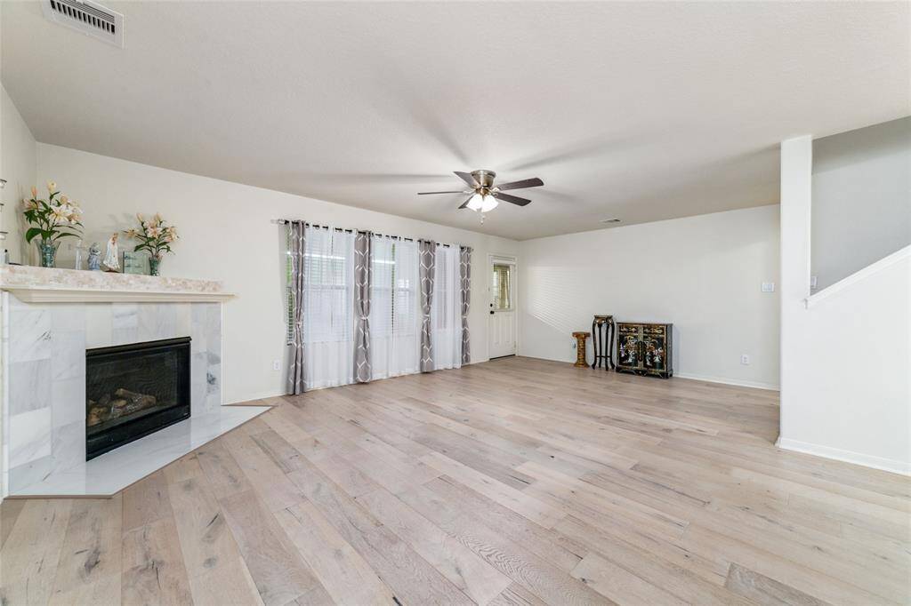 This is a spacious, well-lit living room featuring modern engineered hardwood flooring, a stylish white marble fireplace, contemporary window treatments, and a ceiling fan. The neutral color palette provides a versatile backdrop for personalization.