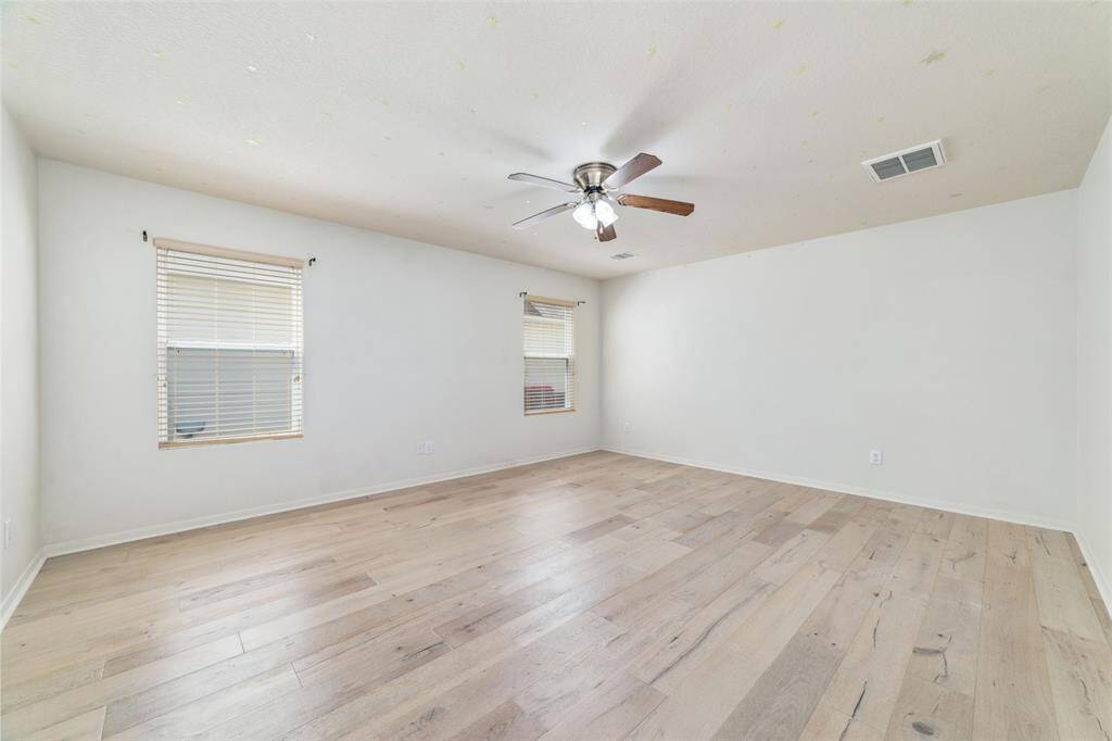 Spacious Primary bedroom on first floor, well-lit room with modern wood flooring, ceiling fan, and two windows with horizontal blinds, offering a clean canvas for personalization.