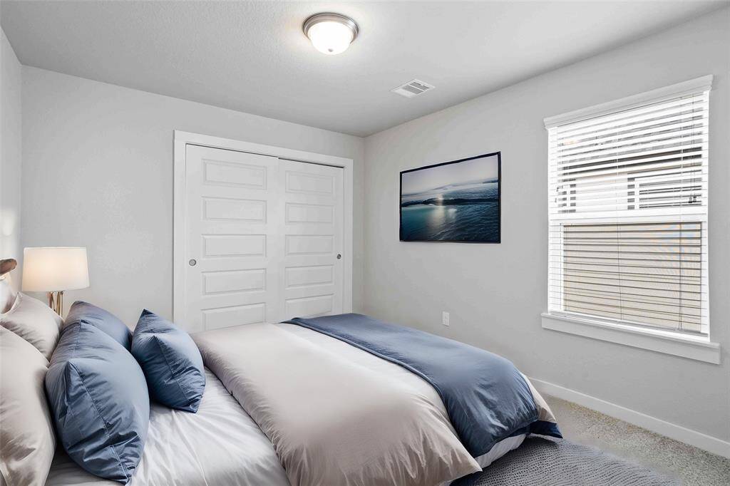 Secondary bedroom features plush carpet, neutral paint, lighting and a large window with privacy blinds.