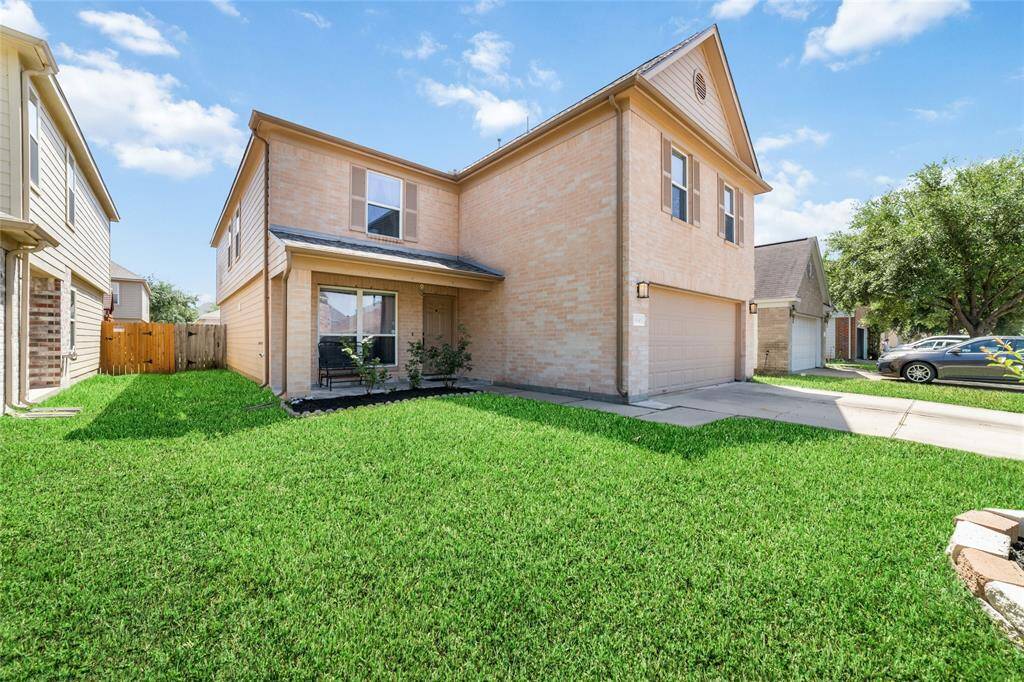 This is a two-story, single-family home featuring a well-maintained lawn and an attached two-car garage. The exterior is finished in a light brick facade, and the property includes front porch