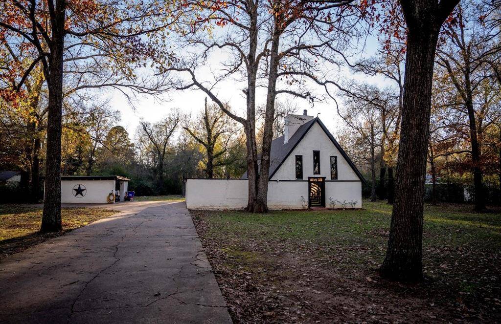 This property features a charming house with a gable roof, surrounded by mature trees. It includes a spacious driveway and a detached garage. The yard offers ample space and a serene, wooded setting.