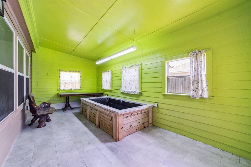 This is a bright, enclosed space featuring vibrant green walls and ceiling, large windows with simple curtains, and gray tile flooring.