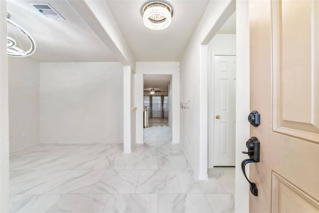 This interior space features tall ceilings with recessed lighting, elegant porcelain floors, and a neutral color palette, providing a bright and open canvas for personalization. The view from the entryway shows a clear line of sight through to additional rooms, and open floor plan.