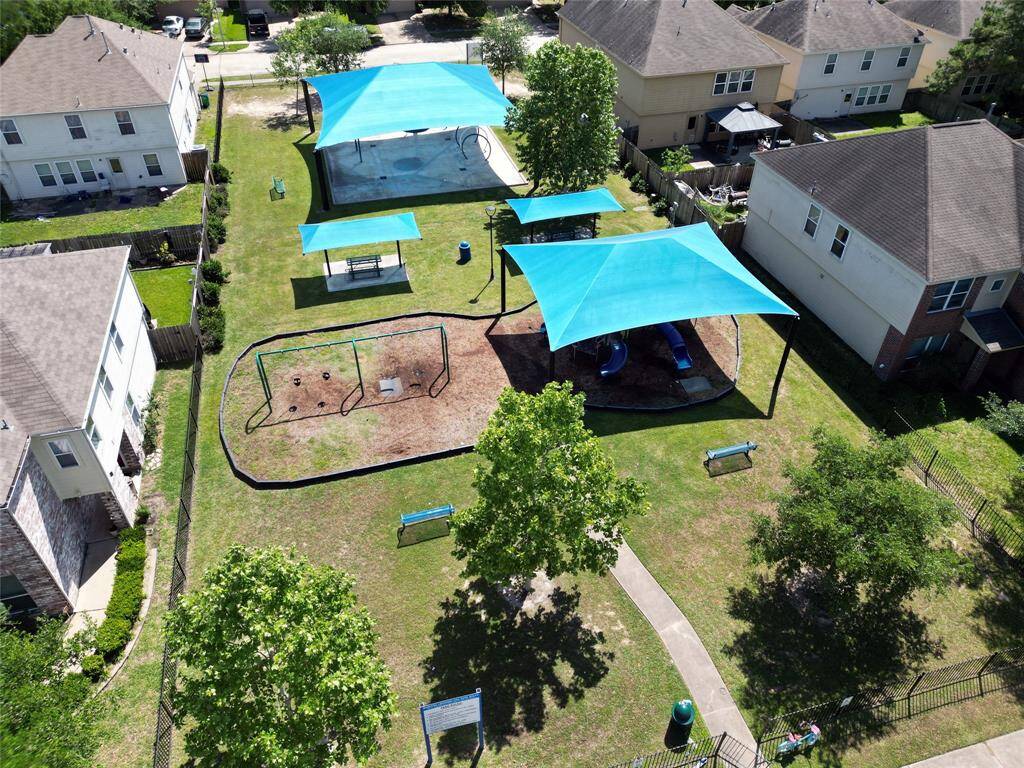 The photo shows an aerial view of a community area with a large shaded picnic tables, and a children's playground with a slide, all nestled between residential buildings, providing a family-friendly outdoor environment.