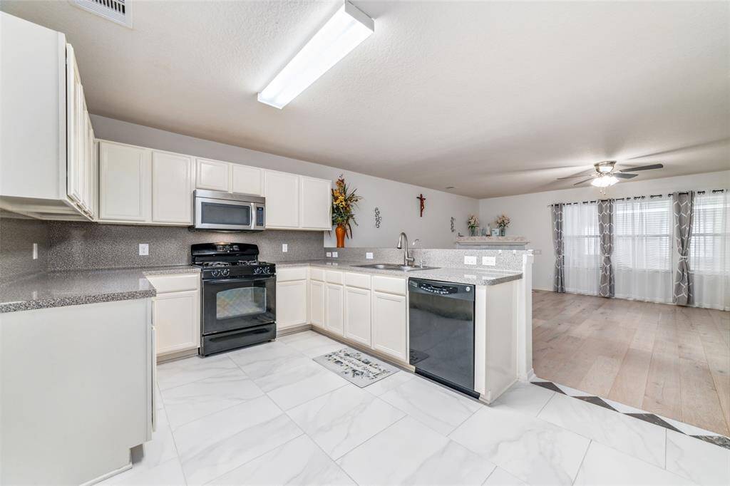 This is a bright, modern kitchen with white cabinetry, stainless steel appliances, and granite countertops. It features porcelain tile flooring, extending into a spacious living area with ample natural light.