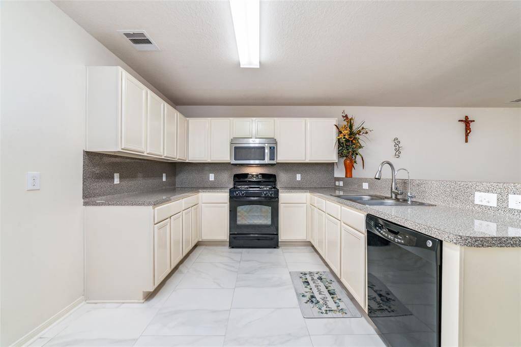This is a bright, modern kitchen with white cabinetry, stainless steel appliances, and granite countertops. It features porcelain tile flooring, extending into a spacious living area with ample natural light.