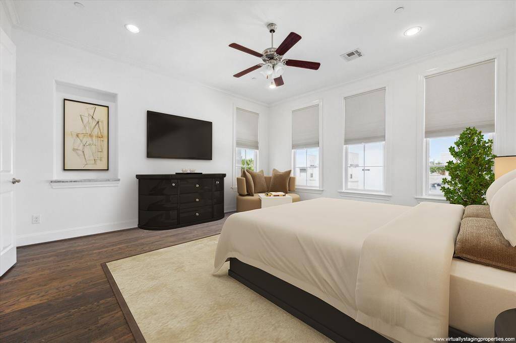 Virtually staged, large, light-filled primary bedroom features hardwood floors and custom window coverings.