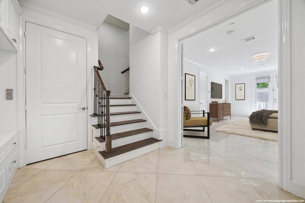 Foyer view toward generously proportioned, virtually staged, versatile first-floor bedroom with en suite bath / living area / office / game room / workout room with flow-enhancing seamless ceramic tiles set on diagonal. Spacious, light-filled room features en suite bath and double door access to verdant, brick-paved patio and low-maintenance, artificially turfed backyard.