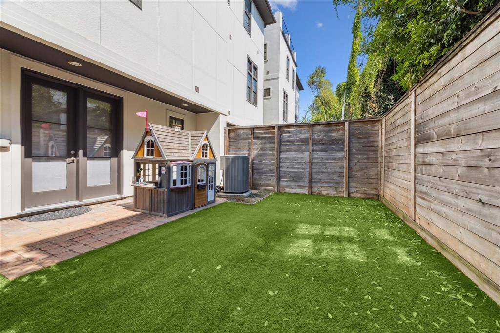 Fenced backyard with low-maintenance artificial turf and brick paver patio.