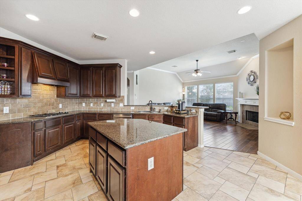 This open-concept kitchen and living area features dark wood cabinetry, a large kitchen island with granite countertops, open to the cozy living room with a fireplace. Lots of natural light