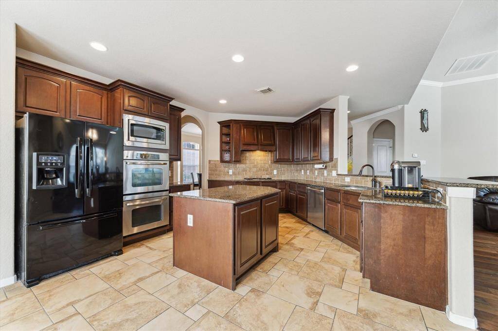 Another view. of the spacious kitchen with rich wood cabinetry, granite countertops, and a central island. Features modern appliances, including a double oven and a large fridge. The open layout flows into the living area, ideal for entertaining.