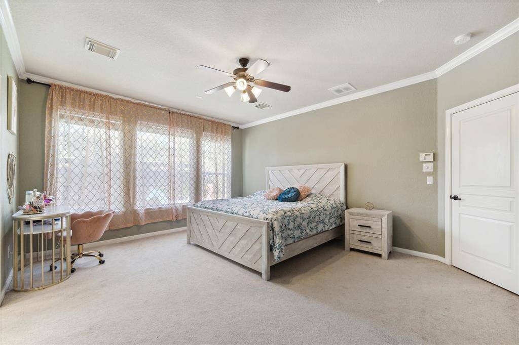 This spacious first floor primary bedroom features large windows with elegant drapes, a ceiling fan, and a neutral color palette.