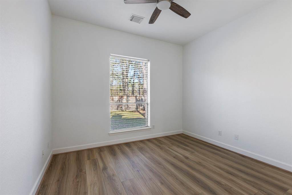This inviting downstairs secondary bedroom features gleaming hardwood floors that promise a seamless flow throughout, complemented by a stylish ceiling fan.