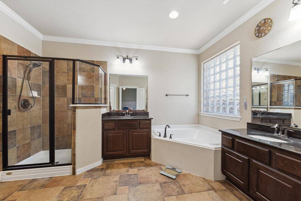 Primary bathroom features a large stand alone shower, a luxurious corner bathtub, dual sinks with dark wood cabinetry, and ample natural light from a frosted glass window.