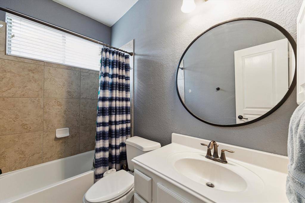 This first floor full bathroom features a modern design with a tiled bathtub, large round mirror, sleek vanity, and natural light from a horizontal window.