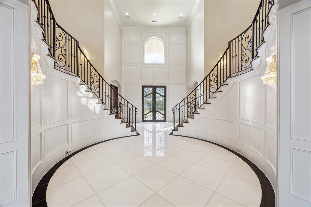 This grand foyer features soaring ceilings, a striking double staircase, and exquisite iron railings, setting the stage for luxury living. Perfect for those seeking a statement entrance in their dream home.