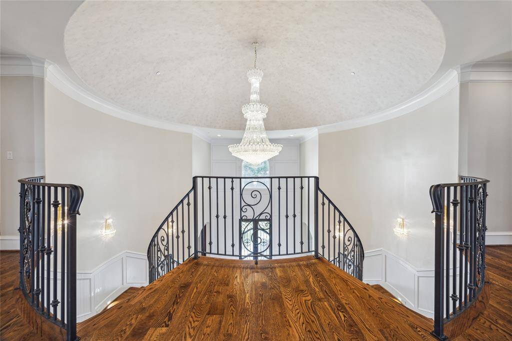The stunning upstairs landing, featuring a grand chandelier and a beautifully crafted wrought-iron staircase, set against rich hardwood floors.