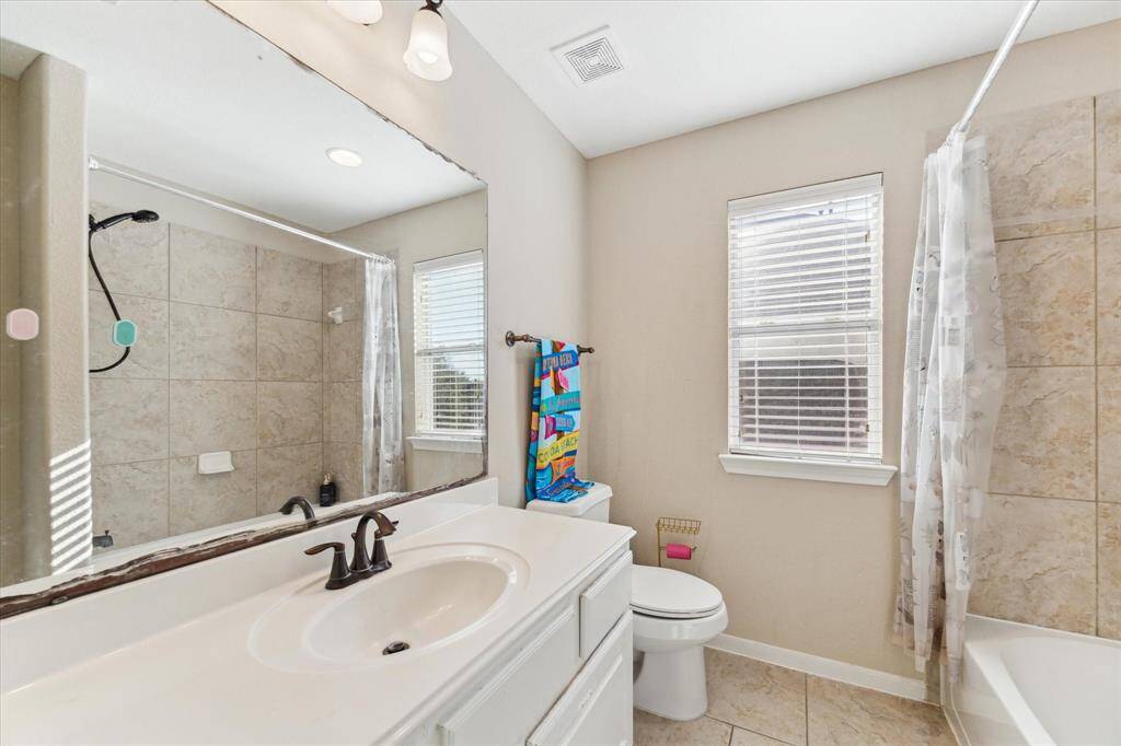 Bright and airy full bathroom on the second floor, featuring a large mirror, single-sink vanity, tiled shower/tub combo, and natural light from a window with blinds.