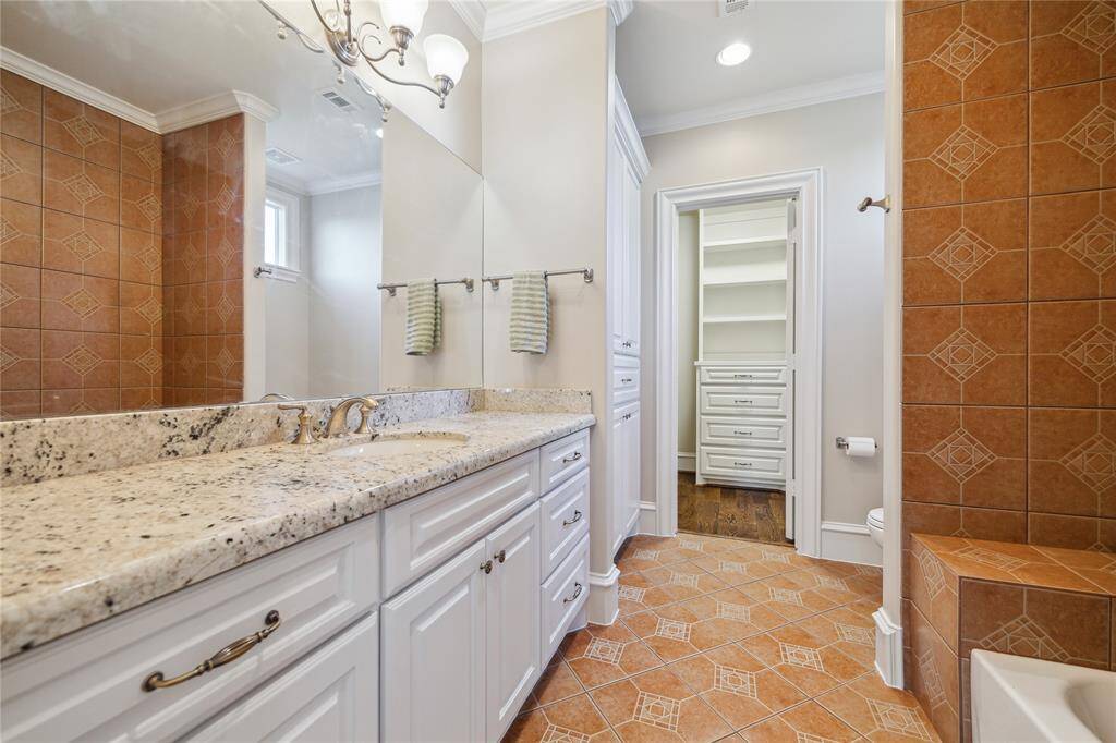 Bathroom featuring a stone countertop and ample storage. The warm tile flooring and coordinated shower tiles create a cozy ambiance, while the walk-in closet offers added convenience.