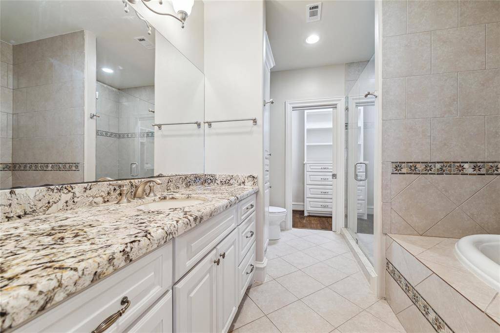 Bathroom featuring a stone countertop, spacious vanity, and a beautifully tiled shower. The built-in storage and sophisticated design ensure both style and convenience.