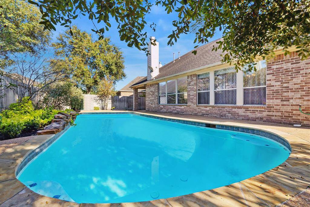 Another view of the charming backyard with a sparkling blue swimming pool, surrounded by serene lush greenery