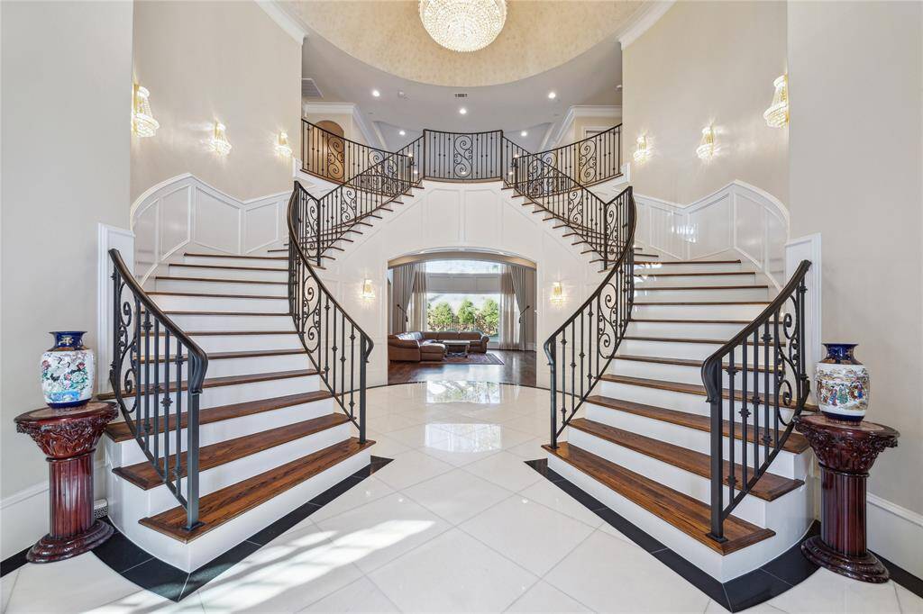 Welcome to your dream home! This grand foyer features an elegant double staircase with intricate iron railings. The space is bright and inviting, with high ceilings and a stunning chandelier, perfect for making a lasting impression.