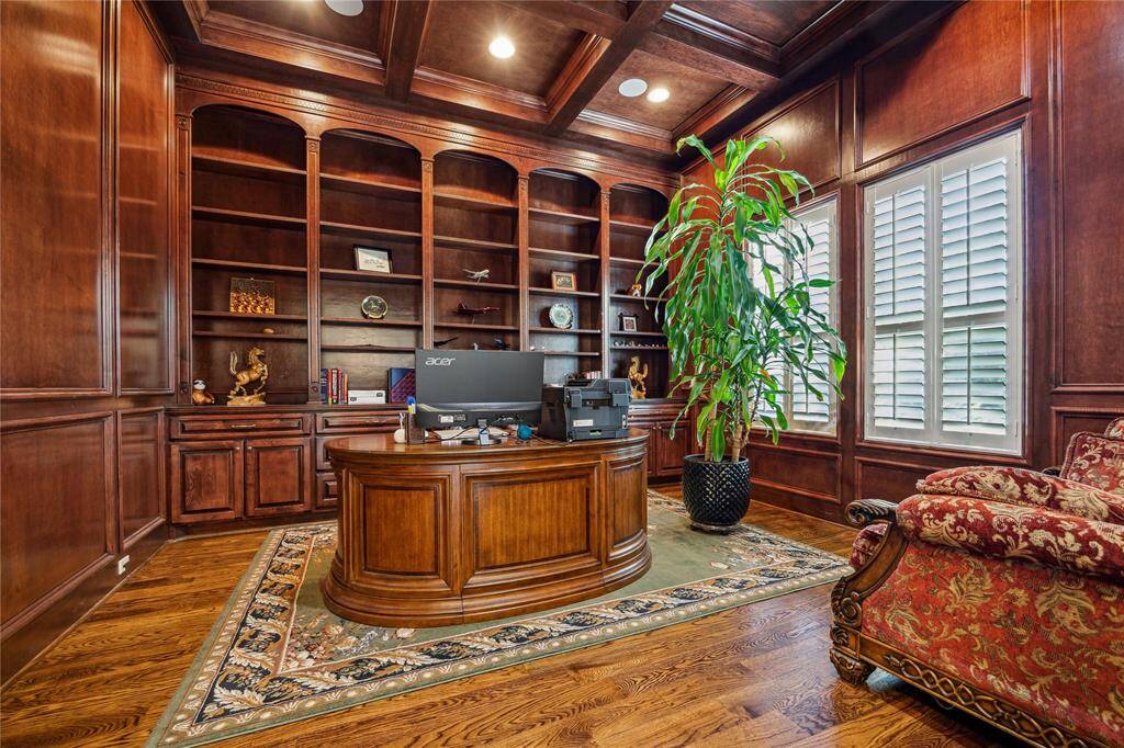 Home office featuring rich wood paneling, built-in bookshelves, and elegant coffered ceilings. Abundant natural light pours in through large windows, creating the perfect environment for productivity and inspiration.