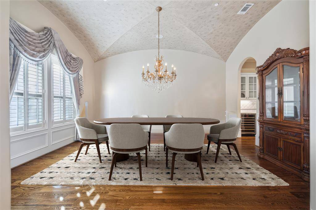 This dining room features a vaulted ceiling, a stunning chandelier, and large windows with classic drapery. Perfect for hosting, it offers a warm and inviting atmosphere with rich hardwood floors. (virtually staged)