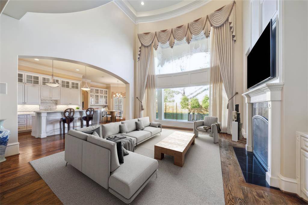 Family room featuring soaring ceilings, expansive windows, and a grand fireplace. The open-concept layout seamlessly connects to a gourmet kitchen, perfect for entertaining. Enjoy abundant natural light and sophisticated design in every corner. (virtually staged)