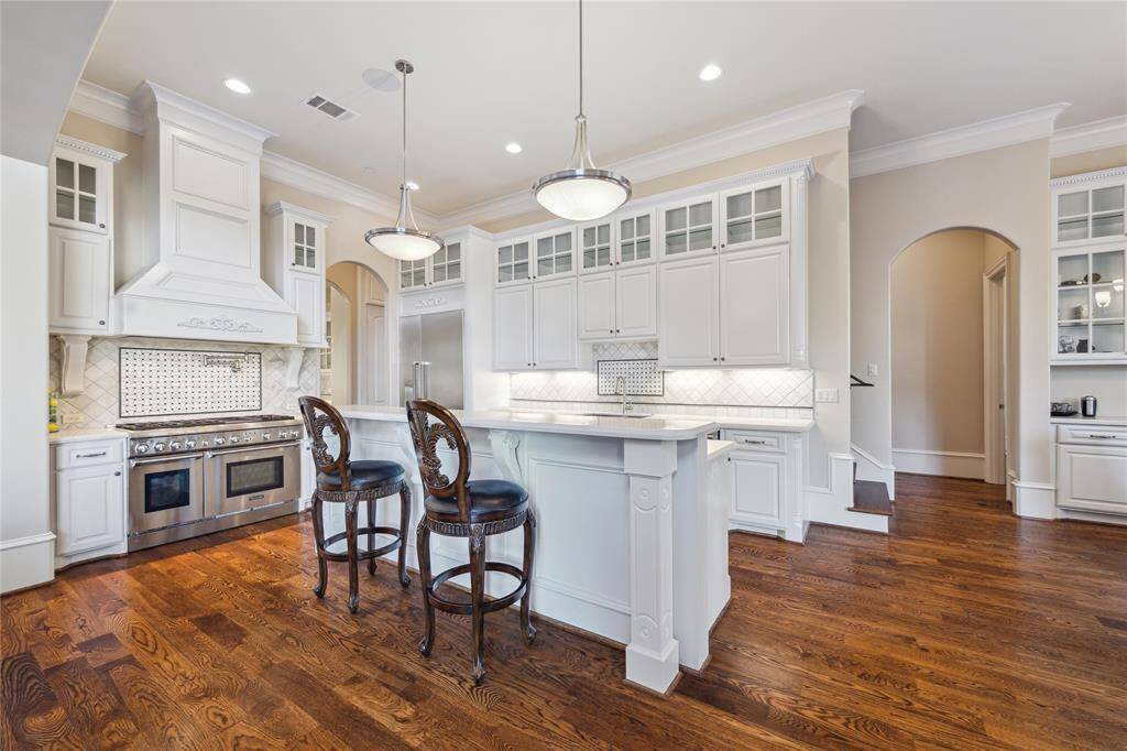 This kitchen features white cabinetry, and a spacious island perfect for entertaining. The open layout and hardwood floors add warmth and sophistication. Ideal for culinary enthusiasts and gatherings.