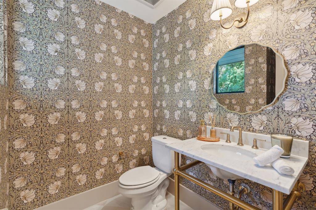 This stunning POWDER ROOM is conveniently situated between the kitchen and family room.  Notice the decorative wallpaper (easy removable wallpaper), beautiful brass leg vanity with carrera marble countertop, new toilet, white and beige checkered porcelain tile floor, decorative mirror and new sconce.