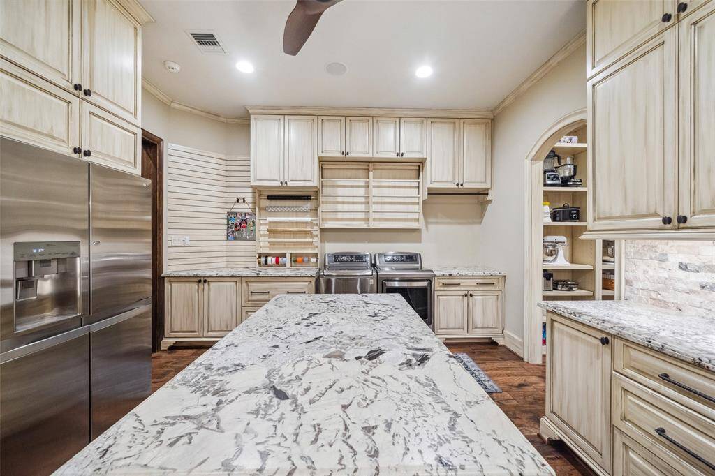 The coveted scullery kitchen is tucked discreetly behind the main kitchen. It boasts a classic farmhouse sink, refrigerator, microwave and additional dishwasher. Abundant cabinetry and an enormous island provide additional storage and versatility. Built-in custom drying racks are situated directly above the washer & dryer and adjacent to the designated gift wrap station. A sizeable walk-through pantry with floor to ceiling adjustable shelving may be accessed from here or directly from the main kitchen.