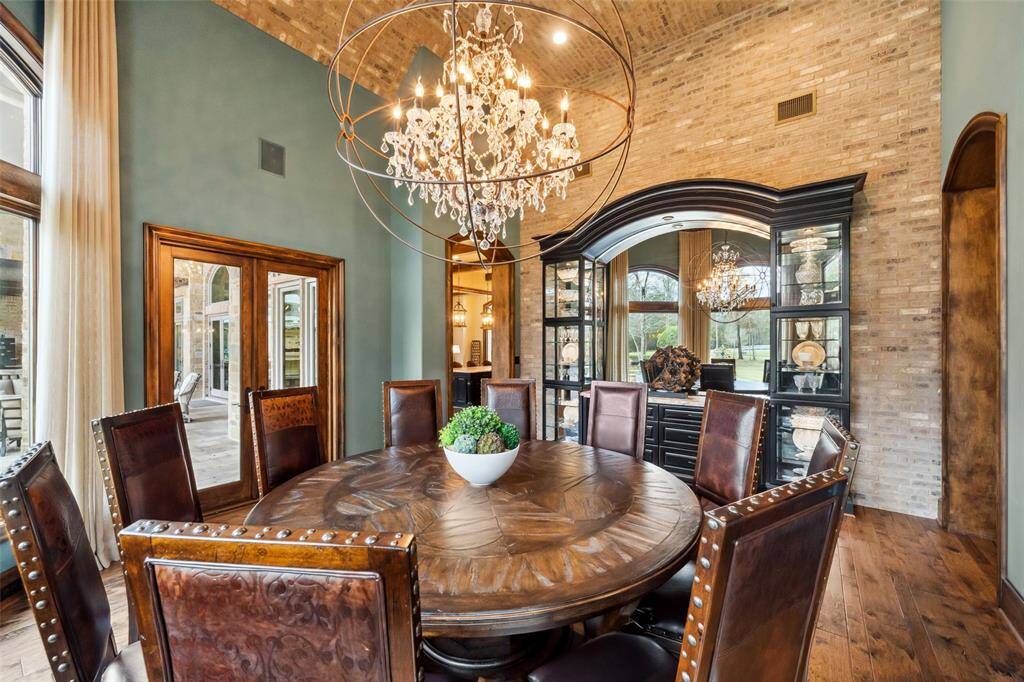 The oversized crystal and iron chandelier casts a warm glow over special celebrations. The dining room features a built-in hutch with glass front display cabinets, storage drawers, lighting and granite counters. The French doors provide easy access to the covered veranda. A masonry wall creates a focal point, soaring 15' to the curved masonry ceiling above.