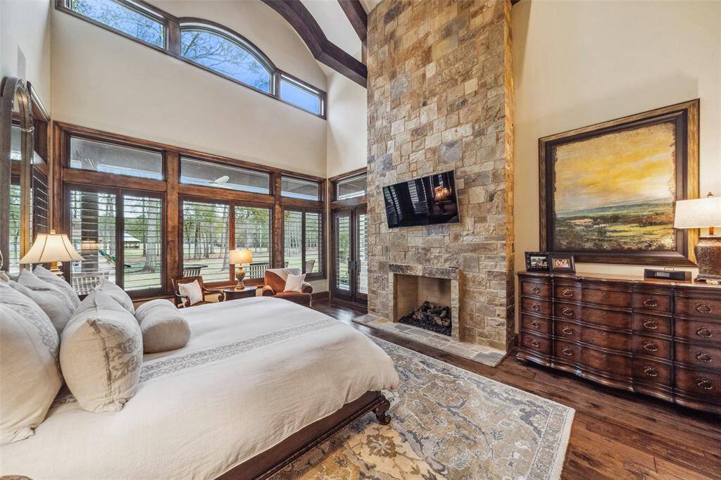 The generously sized primary retreat features a wall of windows showcasing panoramic views of the estate. The retreat is warmed by the gas log fireplace with stonework that soars to the ceiling. French doors provide access to the private, dedicated wrap-around porch, the perfect place to sip your morning coffee in complete solitude.