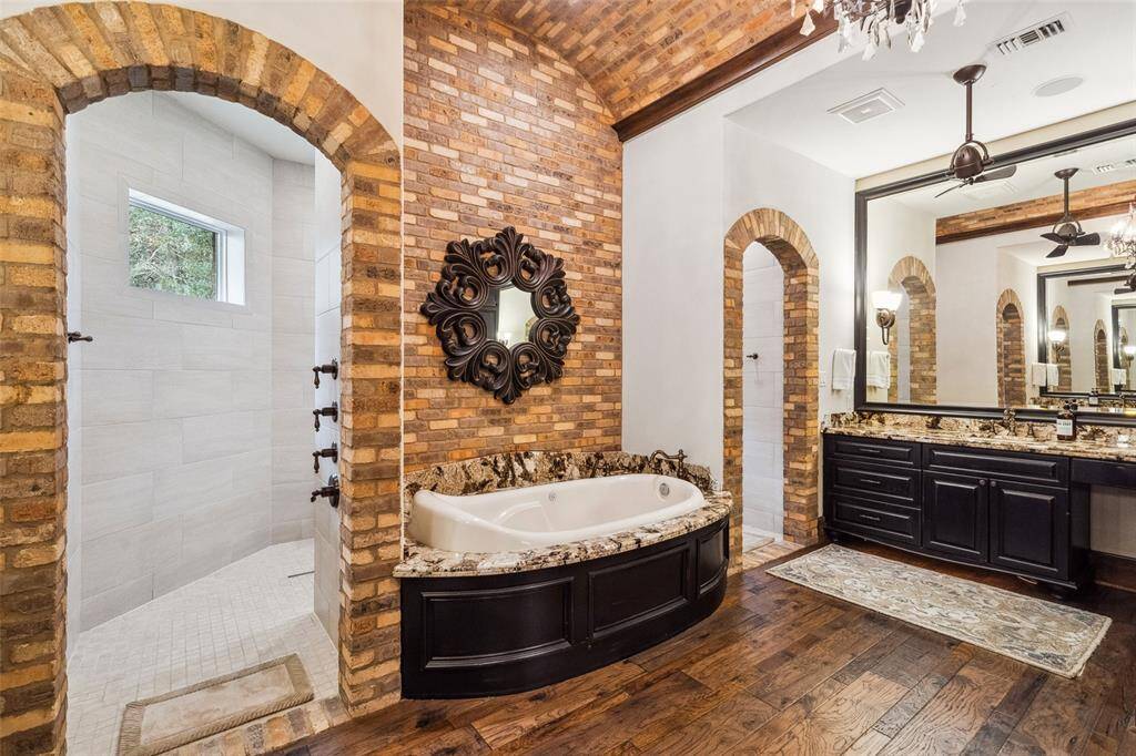 Exposed brick arches define the entrance to the walk-through shower. The spa-like primary bath is detailed with granite countertops, custom crystal chandelier, dual sink vanities, relaxing air-jetted bathtub and enormous walk-in shower that may be accessed from either side of the tub.