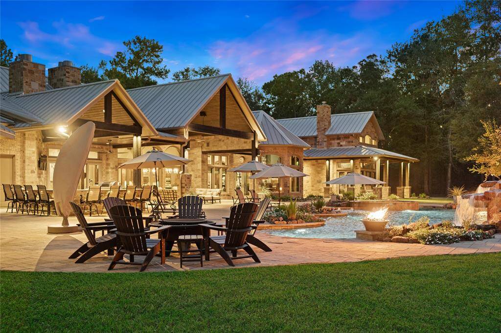 The exterior wood-burning fireplace warms the covered patio on crisp nights while fire bowls surrounding the pool create a warm glow in the evenings. The livable outdoor space for gatherings is vast and features beautiful, expertly placed landscape lighting.