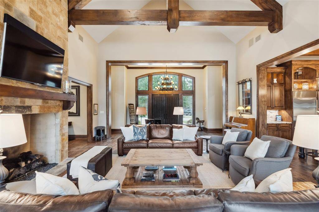 The windows framing the main entry doors provide abundant natural light and a direct line of sight through to the sparkling pool in this open floorplan. The gas log fireplace soars to the vaulted ceiling, highlighting the stonework.