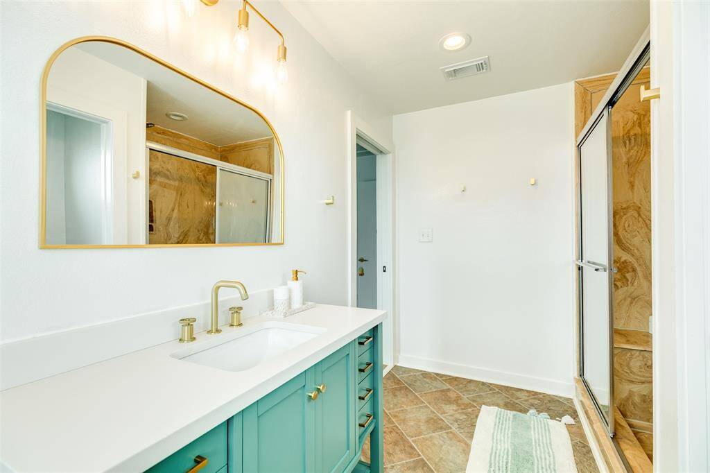 Stylish en-suite bath featuring a modern vanity with gold fixtures, elegant lighting, and a spacious shower. Perfect for relaxation.