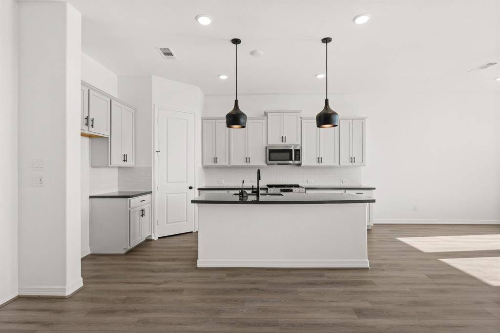 This light and bright kitchen features a large quartz island, white cabinets, a large sink overlooking your family room, recessed lighting, and beautiful backsplash.