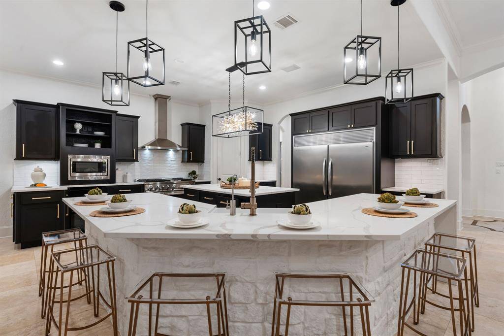 This modern kitchen features sleek black cabinets, stainless steel appliances, and a large central island with a white marble countertop. Stylish pendant lighting and bar stools provide a contemporary touch, making it perfect for entertaining.